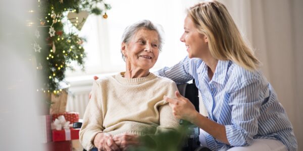 A senior woman in wheelchair with a health visitor at home at Christmas time, talking.