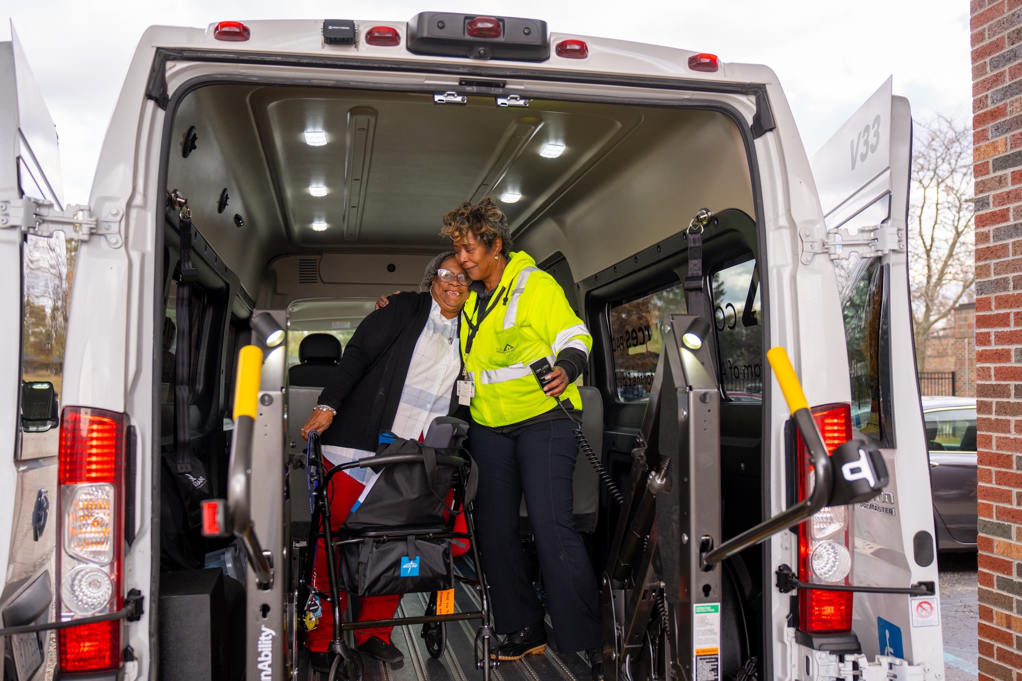 Bus Driver Angie in a side hug with participant Debra while they are standing inside a Care Resources transportation bus