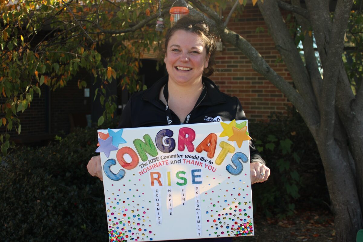 Occupational Therapist Paige Solack smiling outside while holding a poster board that says, "Congrats"