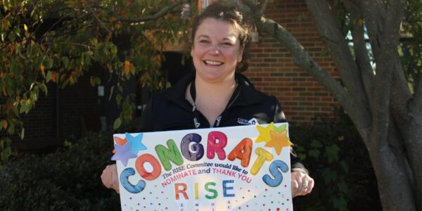 Occupational Therapist Paige Solack smiling outside while holding a poster board that says, "Congrats"